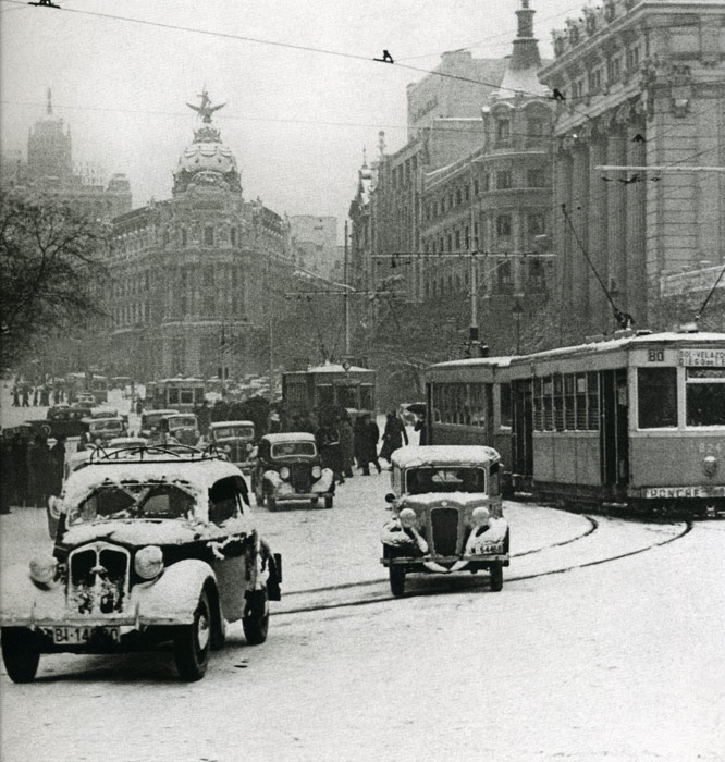 1945. Calle Alcalá junto a Cibeles. Bajo una fuerte nevada un intenso tráfico de coches se desenvuelve junto a los tranvías.