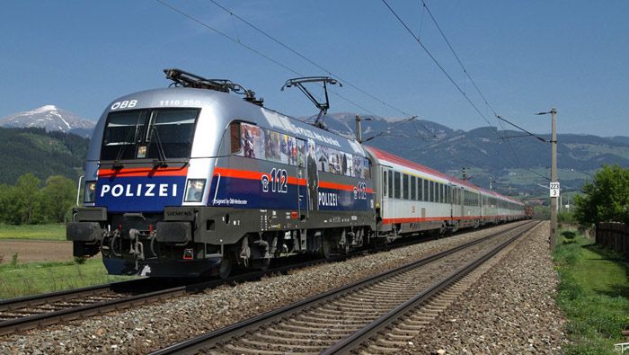 La Taurus 1116-250 austriaca recuerda el número de emergencias para llamar a la Policía, remolcando un tren de Larga Distancia con coches de viajeros y portacoches.