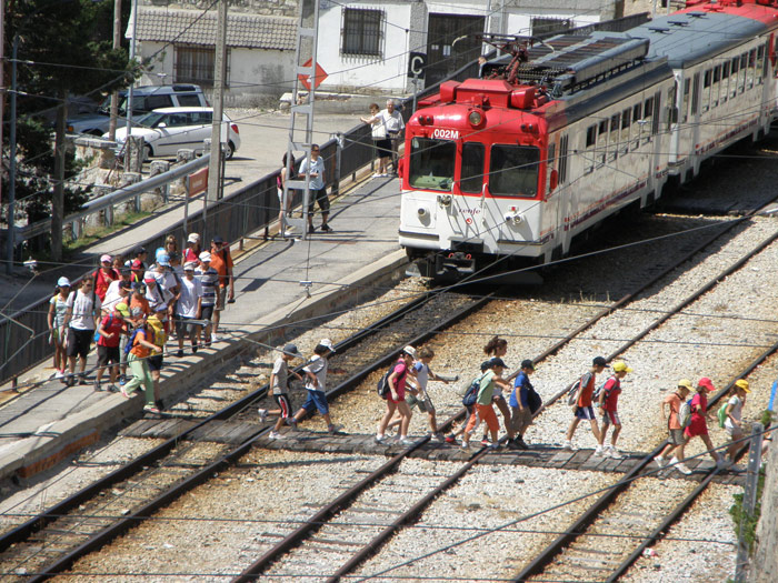 Viajeros cruzan el paso peatonal de Puerto de Navacerrada delante del tren