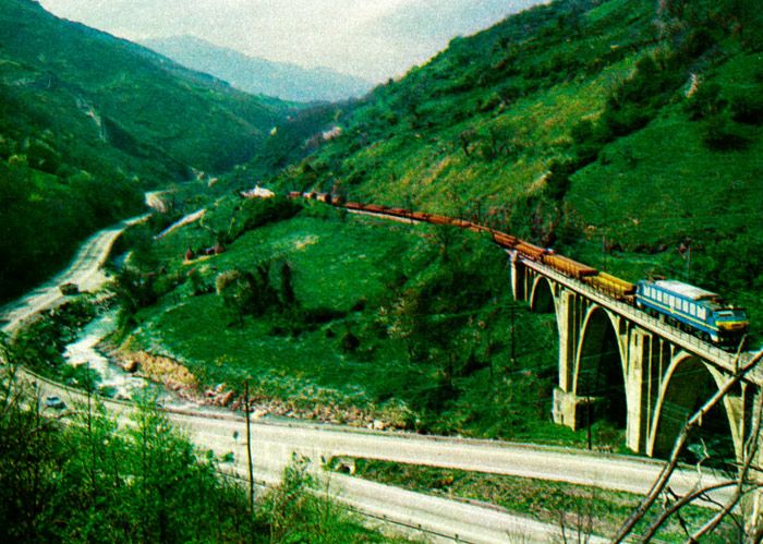 Mercancías con perfiles de acero sobre el viaducto que salva la nacional 630, a la entrada de Puente de los Fierros en Pajares, la obra de ingeniería ferroviaria más ardua de España que celebra su centenario en 1984.